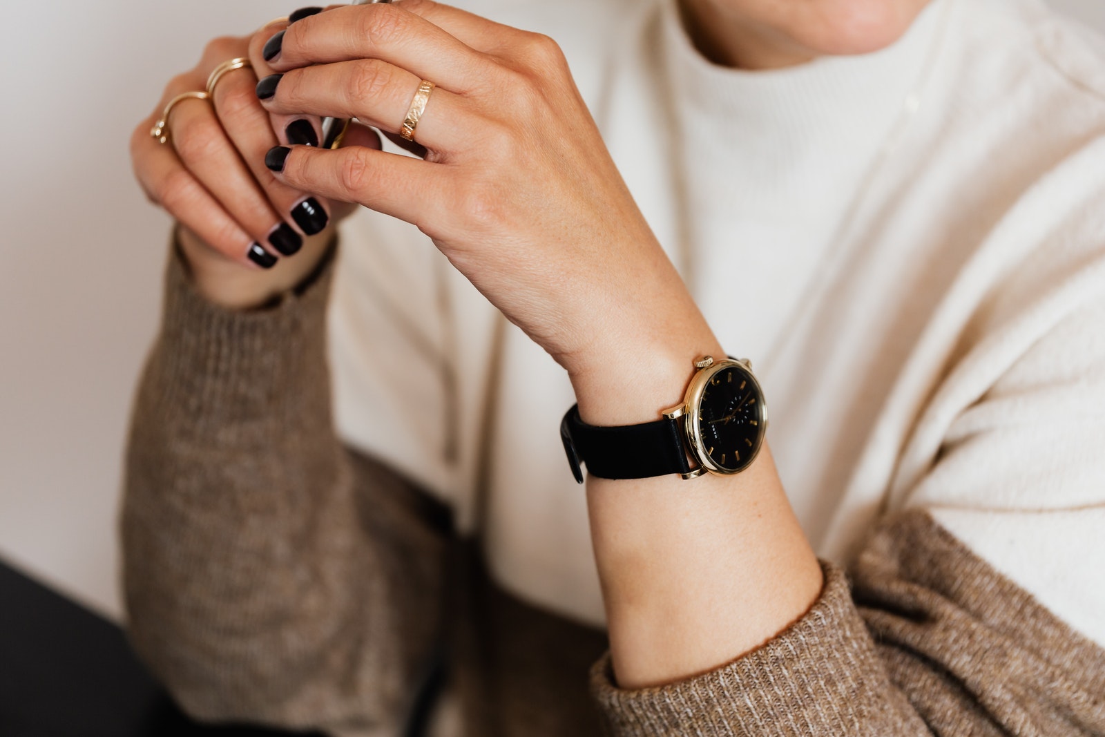 Hands of crop faceless stylish woman with dark manicure wristwatch and gold rings