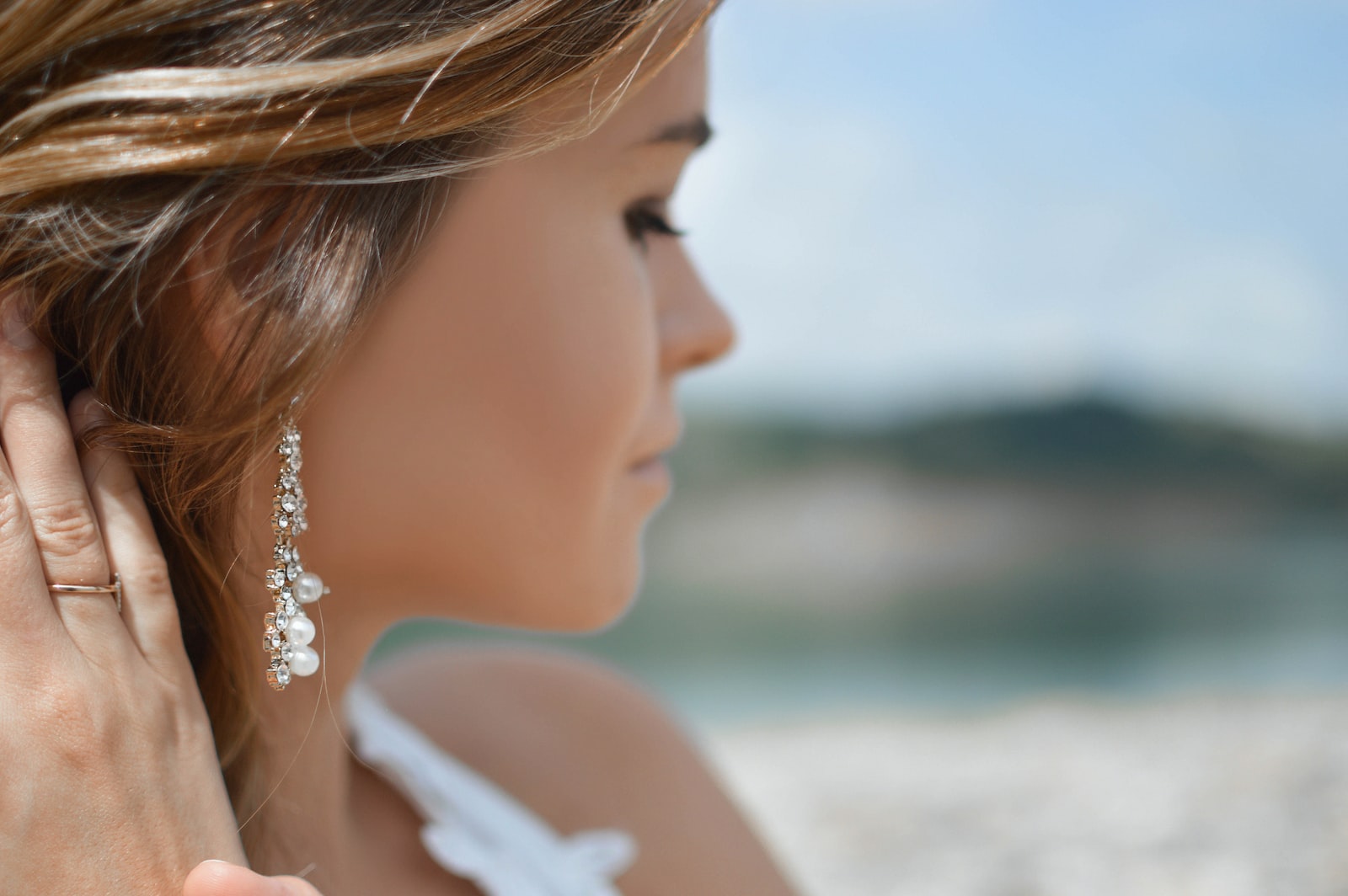 shallow focus photography of woman wearing dangling earrings holding her hair near mountain